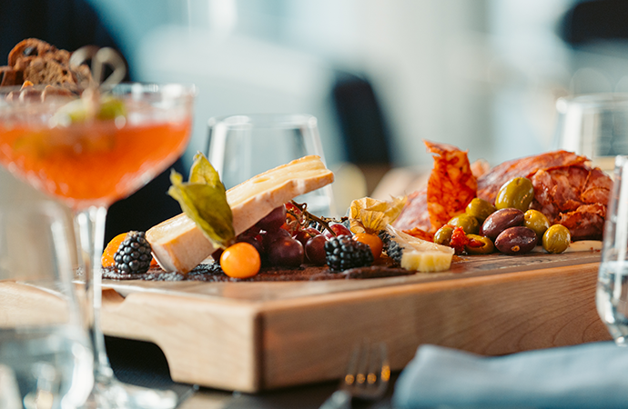 Close-up shot of a charcuterie board with an orange cocktail and water glasses in the background